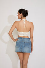 Woman wearing a white lace top and denim skirt against a plain background