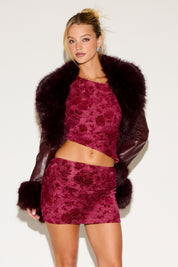 Woman wearing a burgundy floral outfit with a fur-trimmed coat on a white background