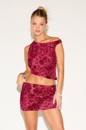 Woman wearing a burgundy floral top and skirt set against a white background