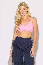 Model is wearing a pink rib knit strap back cami bra top with navy blue pants on a white background. 