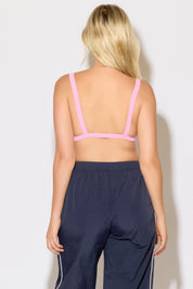 Model is wearing a pink rib knit strap back cami bra top with navy blue pants on a white background. 