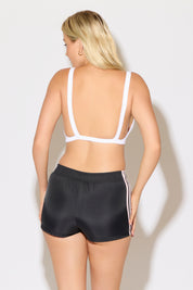 Model is wearing a white rib knit strap back cami bra top with black shorts on a white background. 