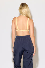 Model is wearing a butter yellow rib knit strap back cami bra top with navy blue pants on a white background. 