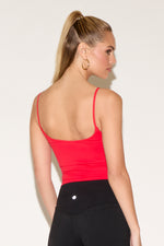 A woman wearing a red tank top, and black leggings stands against a plain, light background.