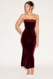 Woman wearing a strapless burgundy velvet dress on a white background