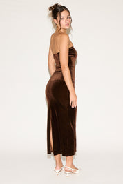 Woman wearing a brown strapless dress with a slit on a white background