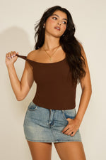 Woman wearing a brown tank top and denim skirt against a plain background