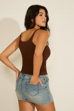Woman wearing a brown tank top and denim skirt against a plain background