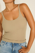 A woman wearing a beige crew neck ribbed trim tunic tank top with a classic crew neck and a fitted silhouette.