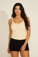 A woman wearing a beige crew neck ribbed trim tunic tank top with a classic crew neck and a fitted silhouette.