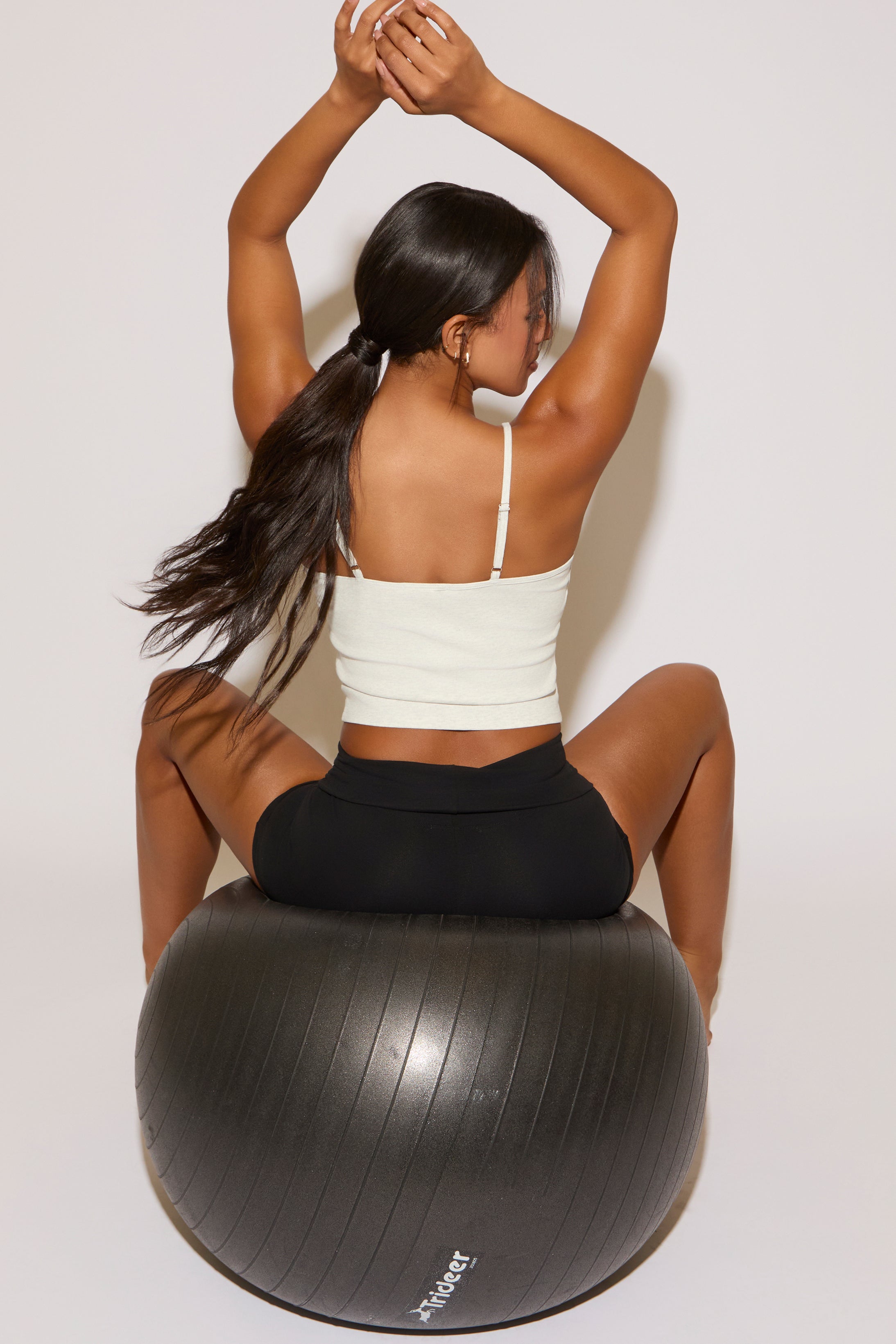 Woman exercising on a black stability ball against a white background