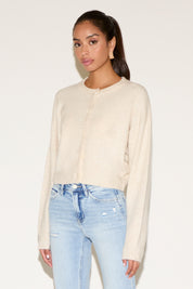 Model wearing a cream button-up cardigan with a relaxed fit, styled with light-wash distressed denim jeans and gold statement earrings, posed against a neutral background.