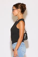 Woman wearing a black sleeveless top and blue jeans against a white background
