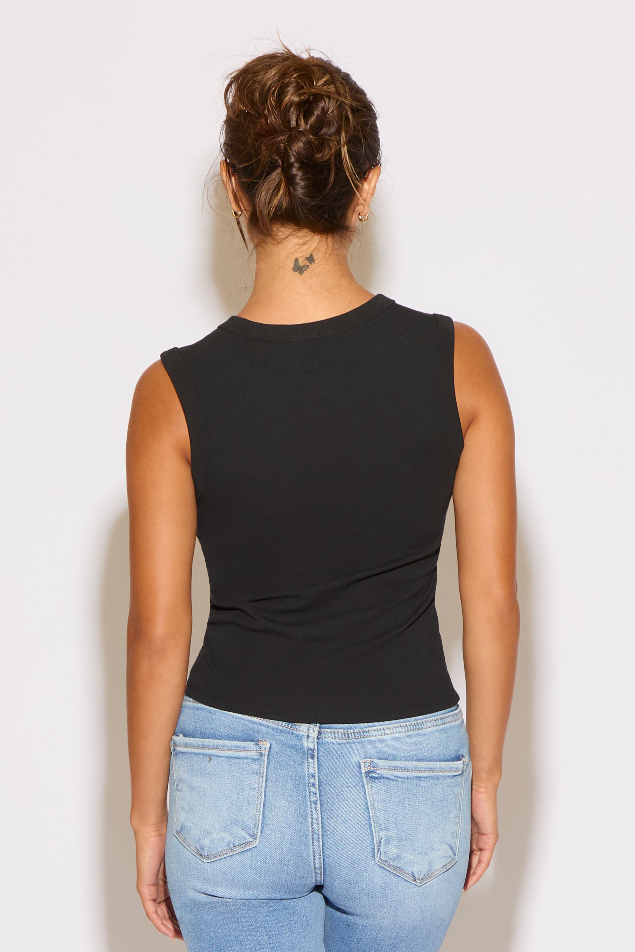 Person wearing a black sleeveless top and blue jeans against a white background