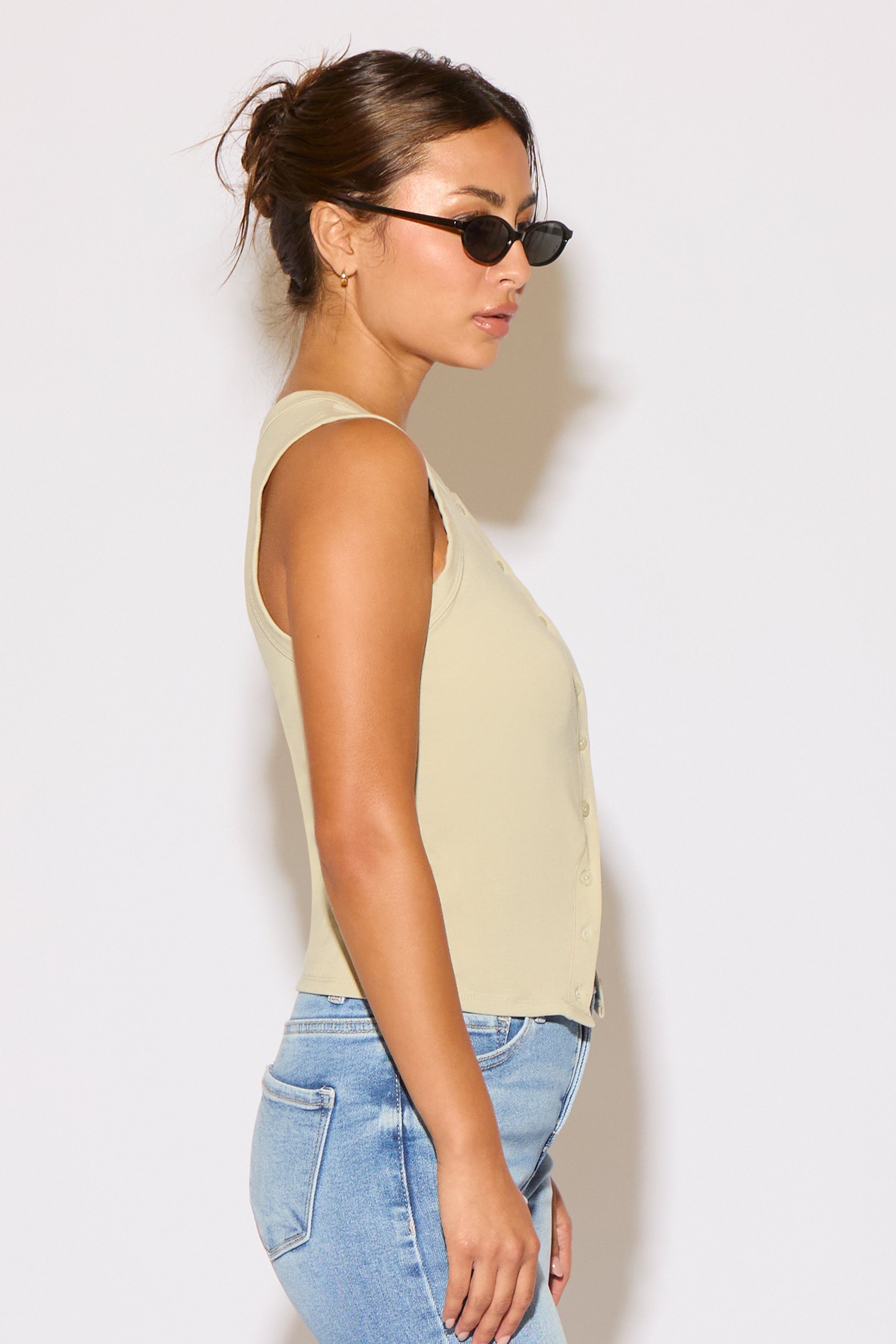 Woman wearing a beige sleeveless top and blue jeans against a white background