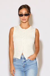 Woman wearing a white sleeveless top and blue jeans against a plain background