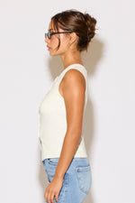 Woman wearing a white sleeveless top and blue jeans against a plain background