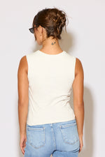 Person wearing a white sleeveless top and blue jeans against a plain background