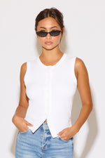 Woman wearing a white sleeveless top and blue jeans against a white background