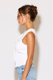 Woman wearing a white tank top and blue jeans against a plain background