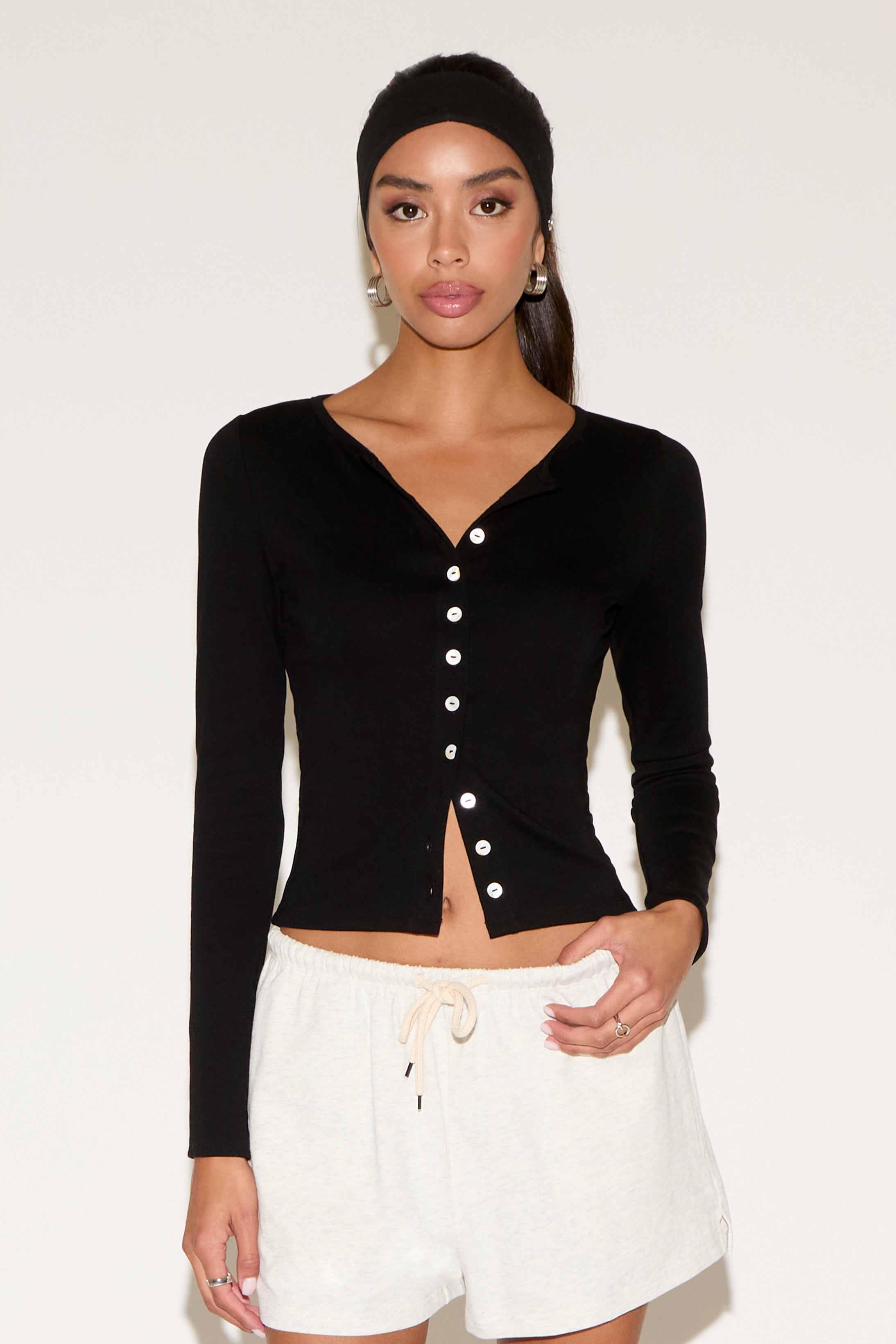 Woman wearing a black long-sleeve cardigan with white buttons and white shorts on a white background