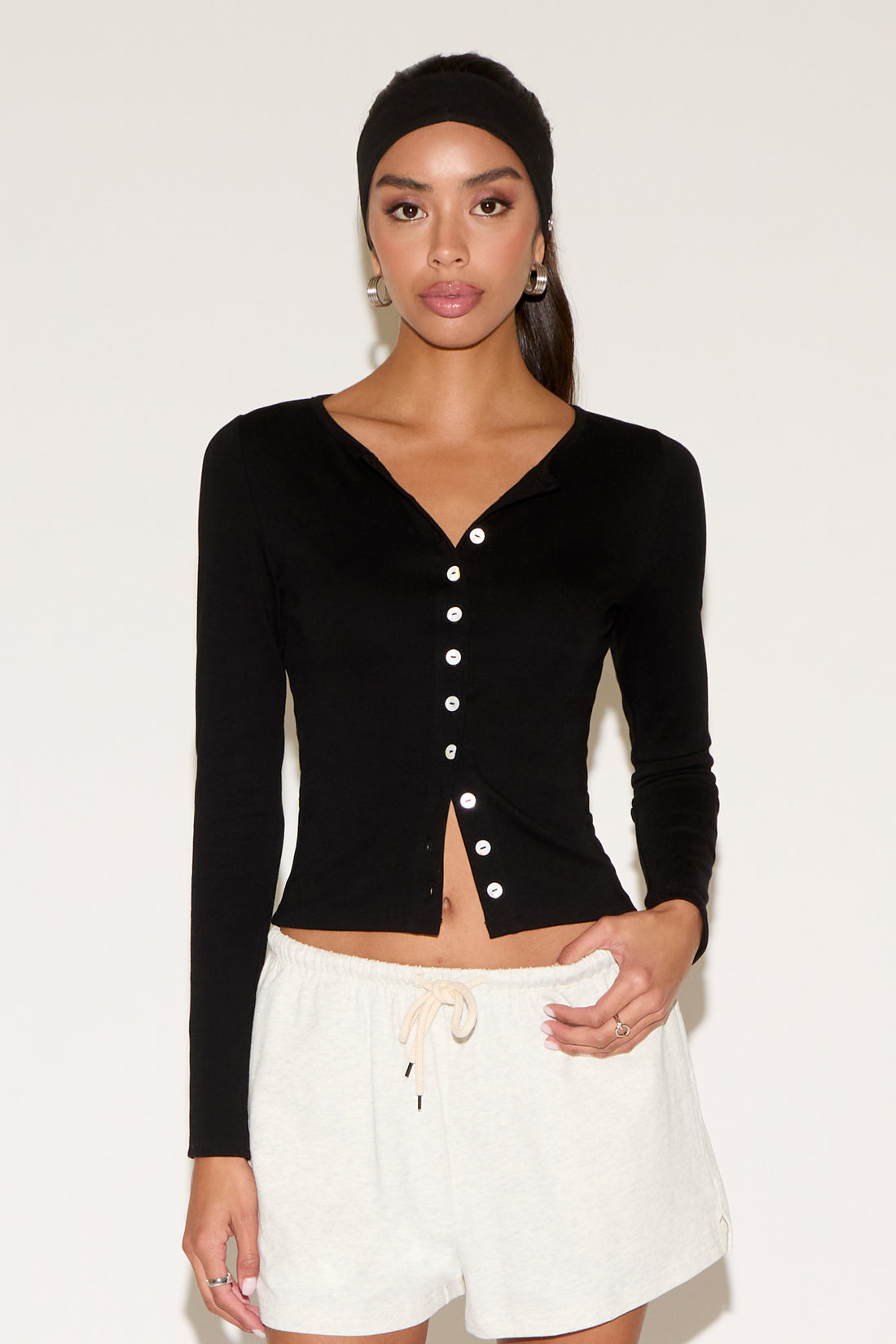 Woman wearing a black long-sleeve top with white buttons and white pants against a plain background