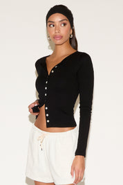 Woman wearing a black long-sleeve crop top and white shorts against a plain background