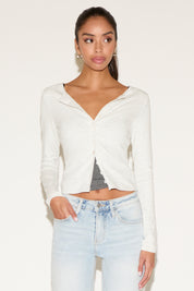 Woman wearing a white long-sleeve top with a knot detail on a plain background