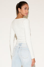 Woman wearing a white long-sleeve top and light blue jeans on a plain background