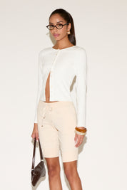 Woman wearing a white cardigan and beige shorts with a plain background