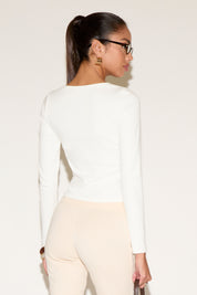 Person wearing a white long-sleeve top and beige pants on a plain background