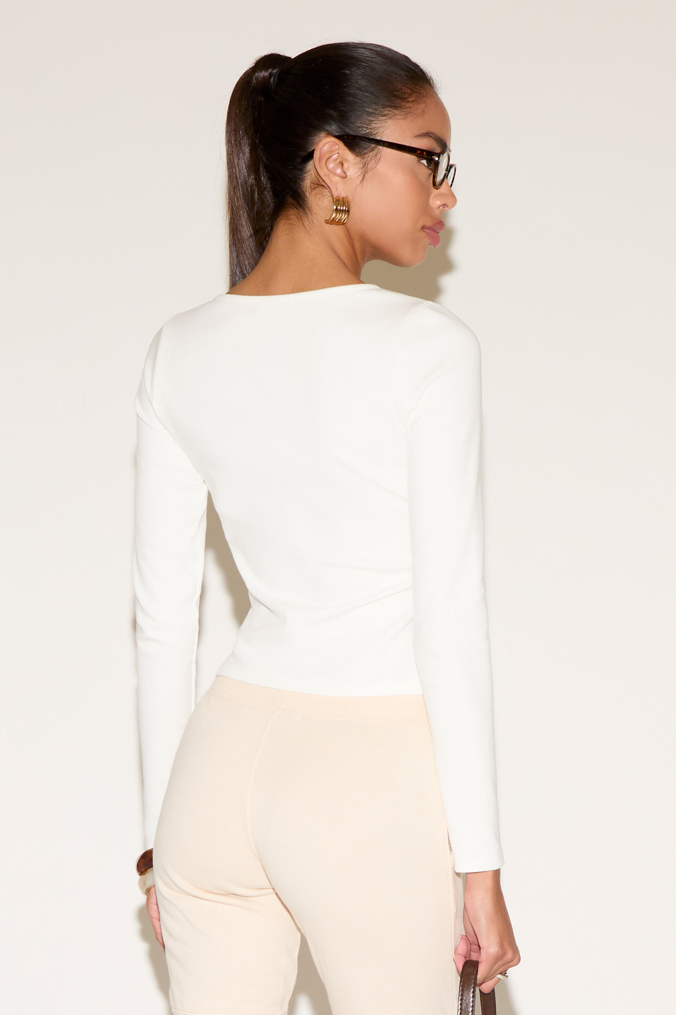 Person wearing a white long-sleeve top and beige pants on a plain background