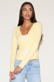 Woman wearing a light yellow cardigan over a white top and blue jeans on a plain background