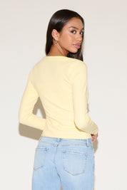 Woman wearing a light yellow long-sleeve top and light blue jeans against a white background