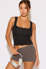 Woman wearing a black tank top and gray shorts holding white headphones against a light background