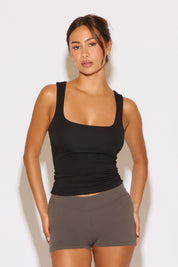 Woman wearing a black tank top and gray shorts against a white background