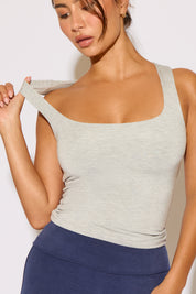 Woman wearing a light gray tank top and blue leggings against a white background