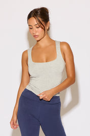 Woman wearing a gray tank top and blue leggings against a white background