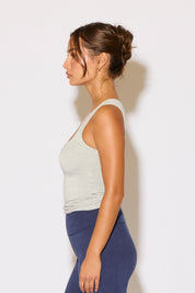 Woman wearing a light gray tank top and blue leggings against a white background