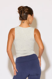 Woman wearing a light gray sleeveless top and blue pants against a white background