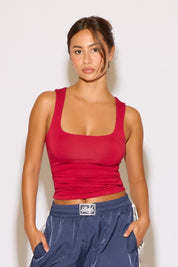 Woman wearing a red tank top and blue pants against a white background