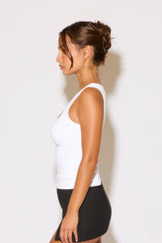 Woman wearing a white tank top and black skirt against a plain background