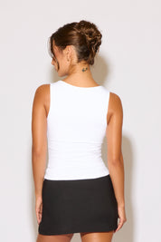 Woman wearing a white tank top and black skirt against a plain background