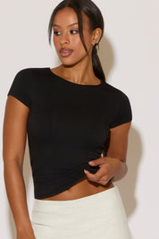 Woman wearing a black top and white pants against a plain background