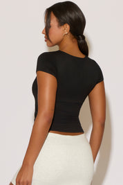 Woman wearing a black top and white pants against a plain background