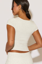 Woman wearing a white crop top and pants against a plain background