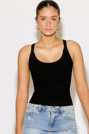 Woman wearing a black tank top and blue jeans against a white background