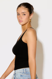 Woman wearing a black tank top and blue jeans against a white background