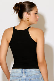 Woman wearing a black tank top and blue jeans against a plain background