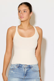 Woman wearing a beige tank top and blue jeans against a white background